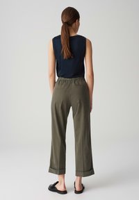 Black sleeveless top paired with olive green wide-leg pants, featuring a drawstring waist and rolled cuffs. Black slip-on shoes.