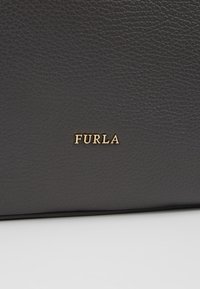 Surface en cuir noir texturé avec petit logo de marque "FURLA" doré embossé au centre.
