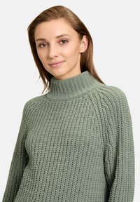 Grüner Strickpullover mit hohem Kragen, der ein strukturiertes Muster und Rippdetails am Hals und an den Bündchen aufweist und eine entspannte Passform bietet.