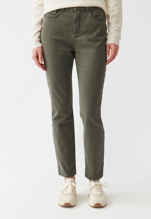 Khaki zelené slim-fit nohavice vyrobené z bavlny s dvoma prednými vreckami, zipsom a kontrastnými švami. Nosí sa s ľahkými teniskami.
