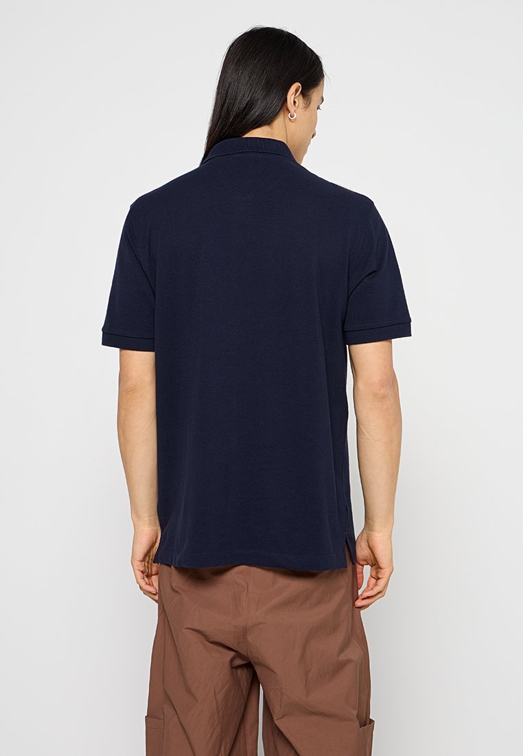 Marineblaues Poloshirt aus weicher Baumwolle, ausgestattet mit einem klassischen Kragen, kurzen Ärmeln und seitlichen Schlitzen für eine bessere Bewegungsfreiheit.