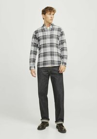 Geweven blouse met ruitjes in grijs en wit, gecombineerd met donkerdenim jeans. De blouse heeft een klassiek kraag en lange mouwen, gedragen met veterschoenen.
