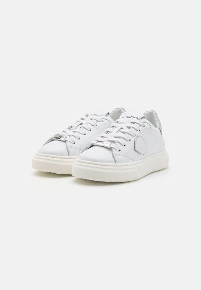 Baskets blanches en cuir avec des détails texturés, des lacets plats, des accents argentés et une semelle en caoutchouc. Design minimaliste avec une toe arrondie.