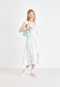 Robe florale blanche avec des fleurs bleues, manches courtes à volants, taille ceinturée, accompagnée d'un sac à main bleu clair et de baskets lavande.