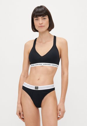 Black sports bra with a V-neck design, featuring a white branded band. Black briefs with a wide white striped waistband. Smooth texture.
