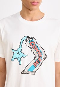 Bílá bavlněná tričko s grafikou modré tekutiny nalévající se z trubice a nápisem "CONVERSE" v červených a modrých akcentích.