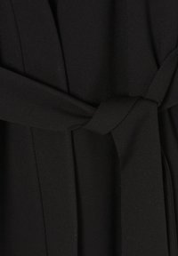 Svart tyg med en slät struktur som har en knyten detalj i midjan. Plagget har en enkel, elegant design med subtila draperingar.