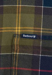Tkanina w kratę w kolorach zielonym, żółtym, granatowym i bordowym. Zawiera małą czarną metkę z napisem "Barbour", wszytą w kieszeń.