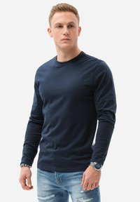 Camicia a maniche lunghe color navy in tessuto morbido, con scollatura rotonda e maniche aderenti. Abbinata a jeans chiari strappati.