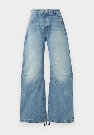 Φαρδιά τζιν με ψηλή μέση σε ανοιχτό μπλε χρώμα, με διαγώνιες ραφές και κλείσιμο με κουμπί, παρουσιάζονται σε λευκό φόντο.