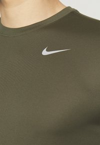 Dettaglio di una camicia verde oliva con il logo Nike swoosh bianco sulla parte sinistra del petto.