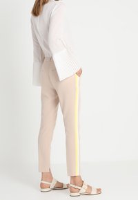 Lightweight white blouse with pleated bell sleeves, paired with beige ankle-length pants featuring a yellow side stripe, and beige sandals.