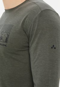 Grünes Langarmhemd mit Rundhalsausschnitt, das eine Berggrafik und vertikale Linien auf der Vorderseite zeigt, aus weichem, strukturiertem Stoff hergestellt.