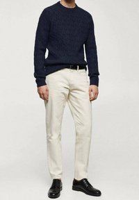 Pull en maille navy avec un motif texturé, pantalon crème et chaussures noires. La tenue est complétée par une ceinture noire.