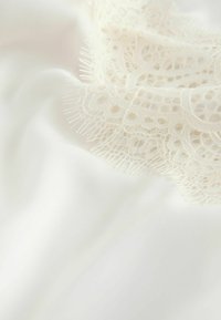 Țesătură albă cu textură netedă, având detalii fine din dantelă ivoire de-a lungul unei margini, cu accente delicate de franjuri.