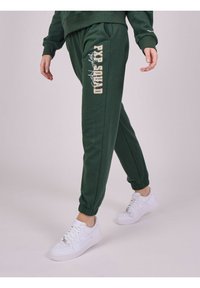 Groene katoenen joggers met elastische manchetten, voorzien van een zijtekstlogo in beige. Gecombineerd met witte sneakers.