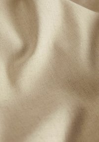 Beige stof met een gladde textuur, met zachte plooien en subtiele schaduwvariaties, wat duidt op een lichte val en flexibiliteit.