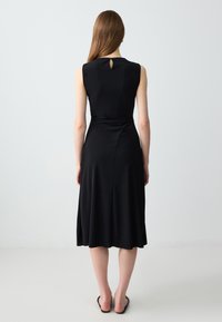 Schwarzes ärmelloses Kleid mit einem taillierten Oberteil und einem ausgestellten Rock, das ein Schlüsselloch-Detail auf der Rückseite und eine glatte Textur aufweist.