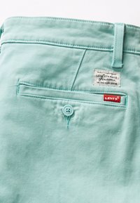 Turkizne Levi's hlače imajo zadnji žep z gumbom za zapiranje, oznako z napisom "Levi Strauss" in gladko bombažno tkanino.