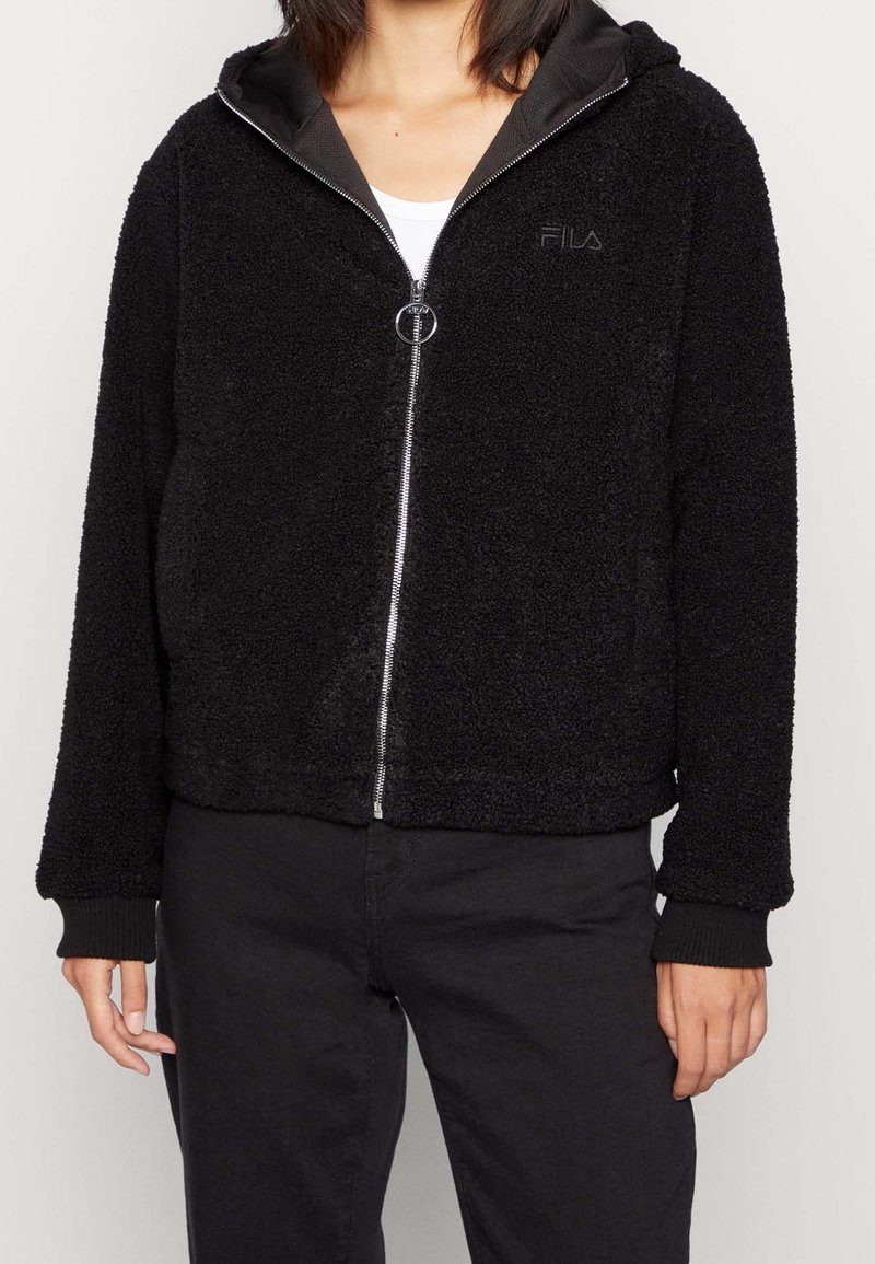 Czarna, puszysta bluza z kapturem zapinanym na zamek, z podszytym kapturem, ściągaczami przy mankietach i srebrnym zamkiem błyskawicznym. Na piersi znajduje się subtelne logo, a powierzchnia ma teksturowaną strukturę.