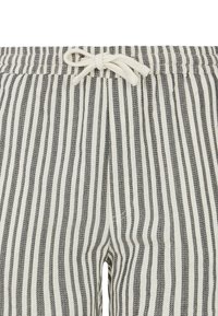 Pantalon rayé beige et noir avec une taille élastique et un cordon de serrage. Présente des rayures verticales et une texture de tissu léger.