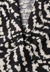 Svartvitt mönstrat tyg med en v-ringad halsringning. Texturen är slät med ett marmorerat mönster som liknar abstrakta former.