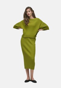 Ensemble deux pièces en tricot côtelé vert comprenant un haut oversized avec des manches larges et une jupe longue jusqu'au mollet, associée à des ballerines noires.