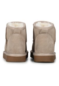 Botines de ante beige con un suave forro de piel sintética blanca, que presentan una forma redondeada, suela plana de goma marrón y detalles de costura.