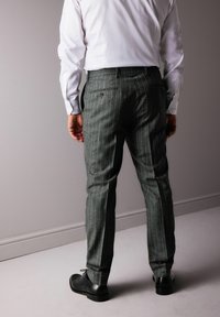 Herren graue Nadelstreifenhose aus strukturiertem Stoff. Verfügt über ein tailliertes Design, zwei Gesäßtaschen und schwarze Schuhe.