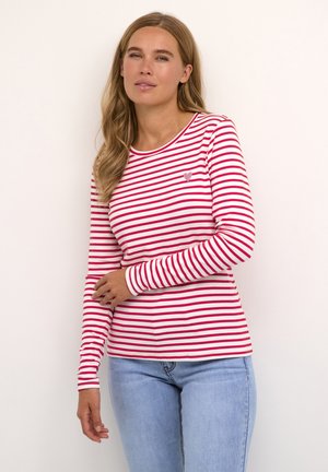 Chemise à manches longues rayée rouge et blanche avec un col rond et un petit emblème en forme de cœur sur la poitrine. Le tissu semble lisse et léger.