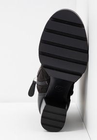Botte de cheville noire avec une tige texturée, dotée d'une fermeture éclair sur le côté et d'une semelle en caoutchouc épaisse avec des rainures horizontales pour l'adhérence.
