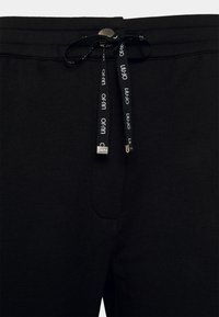 Svarta sweatshirtbyxor i mjukt tyg har ett elastiskt midjeband med dragsko, en framficka och silverfärgad hårdvara på dragskon.