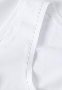 Gros plan d'un débardeur blanc en coton plié montrant une texture lisse et des coutures cousues.