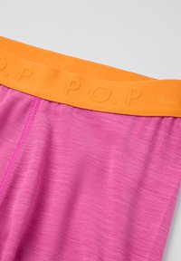 Vaaleanpunaista kangasta, jossa on oranssi vyötärönauha, jossa on kohokuvioitu "P.O.P" -teksti ja näkyvät sauman ompeleet vasemmalla puolella.