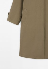 Lang beige trenchcoat-ærme og nederste halvdel, med en rektangulær sidelomme og ren syning på en hvid baggrund.