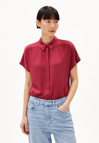 Bordeaux kleurige korte mouw blouse met een kraag, gladde textuur, knoopsluiting aan de voorkant, gecombineerd met lichtblauwe hoge taille jeans.
