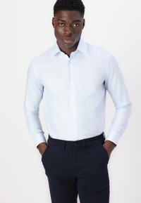 Light blue long-sleeve shirt with a classic collar and button front. Paired with dark blue pants, showcasing a tailored fit.