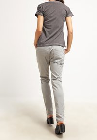 Camiseta gris con mangas enrolladas, combinada con pantalones slim-fit gris claro y zapatos de tacón negro, vista desde la parte trasera.