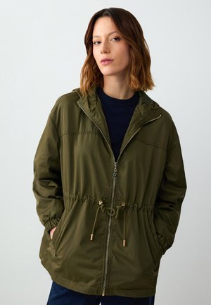 Veste à capuche vert olive avec fermeture éclair, taille ajustable par cordon de serrage, poignets élastiques et poches. Fabriquée en matériau léger et lisse.