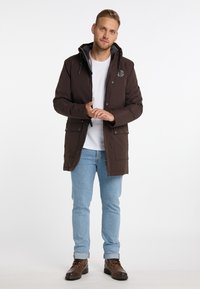 Brun hættetrøje med lynlås foran, sidelommer og logodetalje, parret med lys blå jeans og brune støvler.