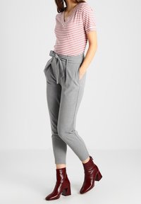 Gestreepte top met korte mouwen in roze en wit. Grijze high-waisted broek met een strik. Glanzende bordeauxrode enkellaarsjes met een chunky hak.