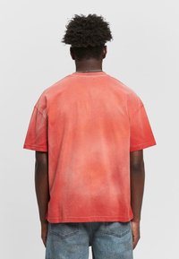 T-shirt en coton tie-dye rouge avec des manches courtes, coupe décontractée et col rond. Le tissu présente un dégradé de teintes rouges allant des plus claires aux plus foncées.