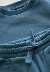 Lys blå sweatshirt med en ribbet rund hals, blød tekstur og en elastisk talje med en bundet snøre detalje.