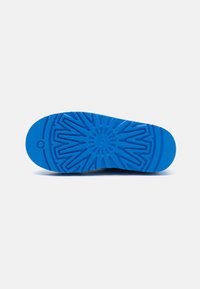 Semelle de chaussure en caoutchouc bleue avec un motif de grip texturé, présentant un design en rayons de soleil central et un bord de bout arrondi.