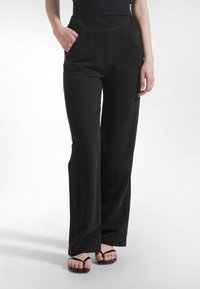 Musta leveälahkeiset housut, joissa on sileä pinta, etutaskut ja korkea vyötärö, yhdistettynä mustiin varvassandaaleihin.