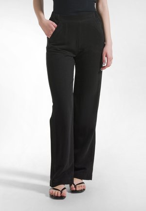 Czarne spodnie o szerokich nogawkach, gładkiej fakturze, z przednimi kieszeniami i wysokim stanem, zestawione z czarnymi klapkami.