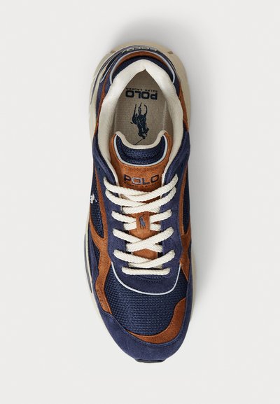 Zapatilla de malla azul marino y gamuza marrón con cordones blancos, que presenta un logo de "Polo" en la lengüeta y un notable emblema de caballo en el costado.
