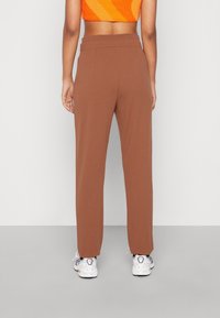 Bruine, hooggewaisted broek met een rechte snit en een gladde textuur, gecombineerd met witte sneakers. Zichtbaar cropped oranje top op de taille.
