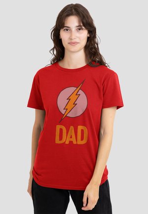 Young woman with long brown hair wearing a red t-shirt with an orange lightning bolt and the word "DAD" in orange letters.