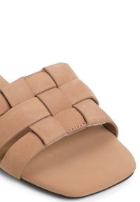 Sandalo scivoloso intrecciato color beige con suola piatta, materiale scamosciato morbido e design delle cinghie intrecciate. Tessuto liscio con dettagli hardware minimi.